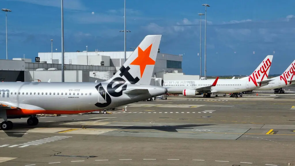 Jetstar Asia aircraft at Changi Airport gate, with Virgin Australia planes in the background on the tarmac.