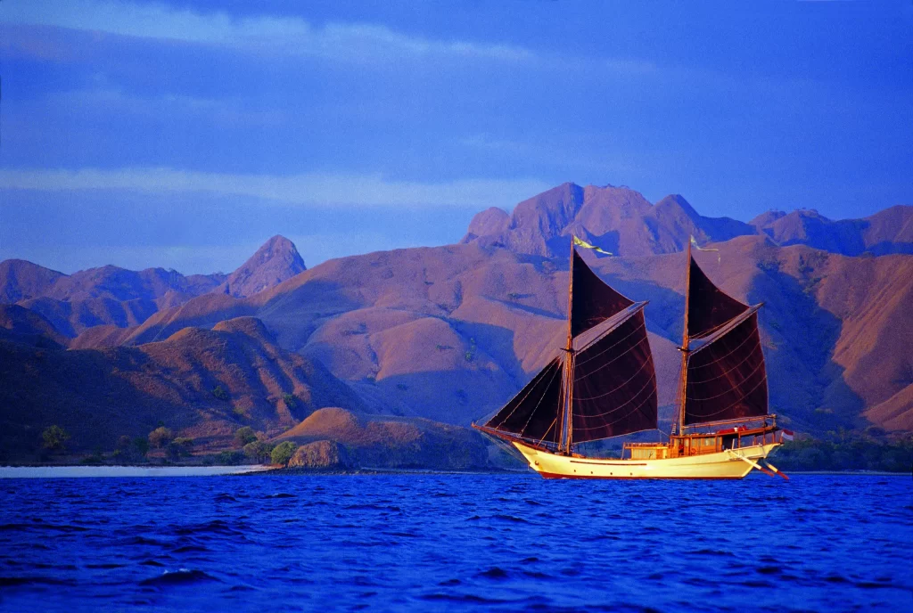 Anne Bonny with her black sales hoisted against the backdrop of Komodo Island Indonesia. 